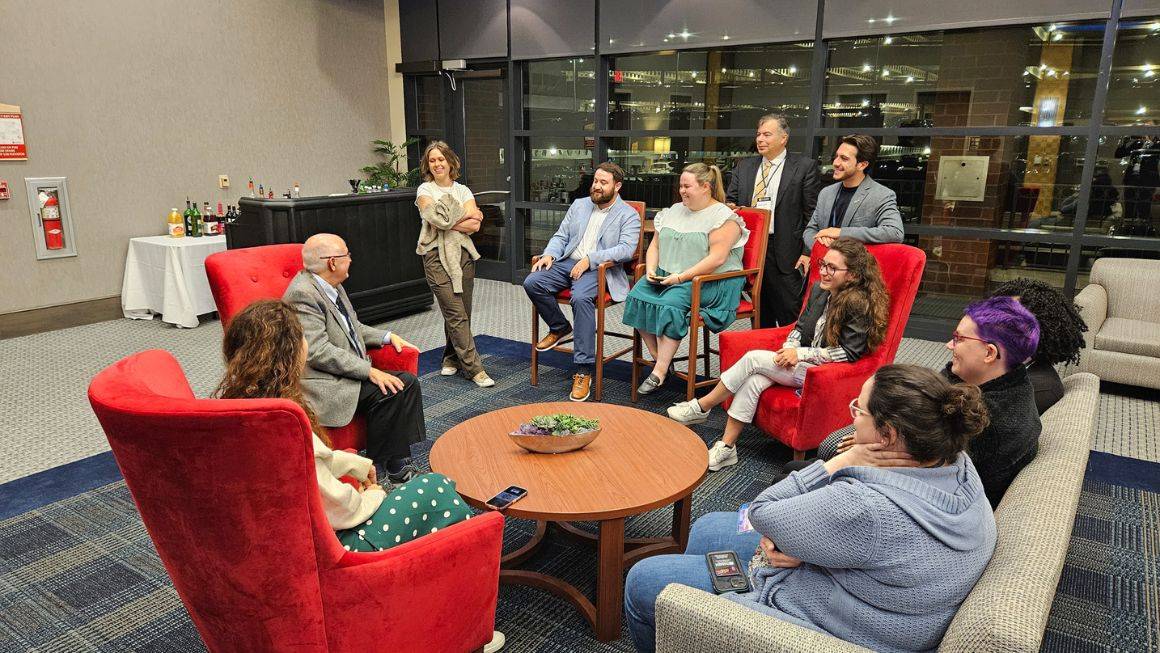 A group of attendees sitting in a circle of chairs conversing with each other.