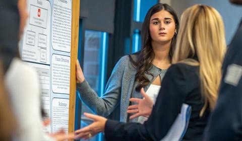 A student presents her research poster to faculty and peers during an academic event.