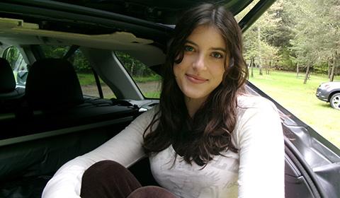 Charlotte Shields-Rossi smiles while sitting in the open trunk of a car, surrounded by trees, during her move to Pittsburgh.