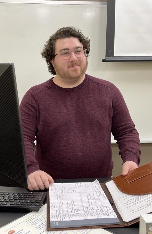 Male student practicing public speaking skills with notes during a debate team session.