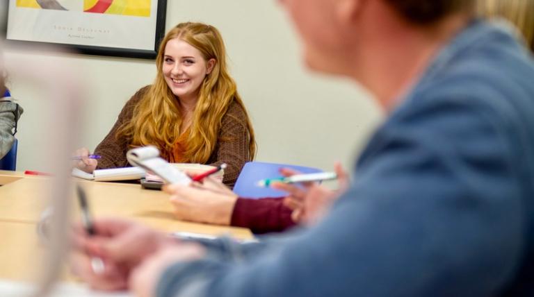 Psychology classroom with students around a table reviewing textbook and notes.