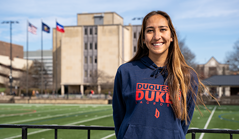 Tristen Chang smiles in front of Rooney Field with College Hall in the background.