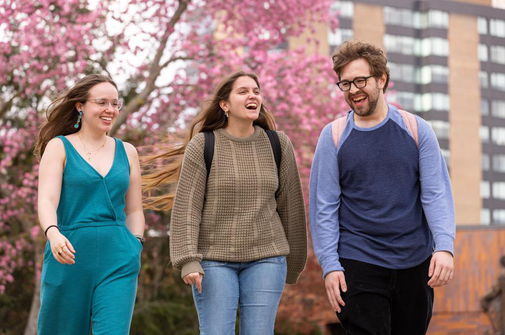 Three Duquesne students walking outside on campus with cherry blossoms in the background