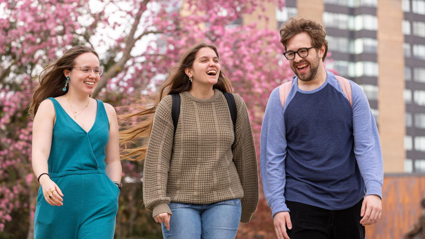 Three Duquesne students walking outside on campus with cherry blossoms in the background