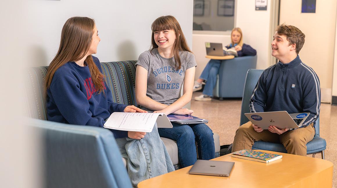 Three students discuss classwork in College Hall lobby.