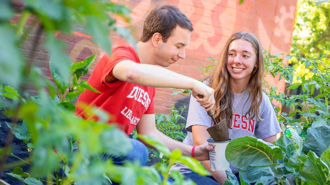 Two students kneeling and filling up a plastic pot in the community garden.