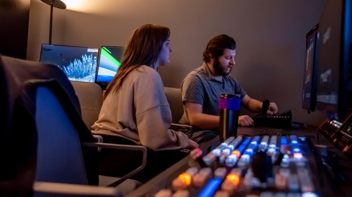 Two students in the broadcast studio editing a video.