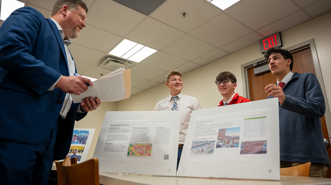 Three students present research posters to professor.