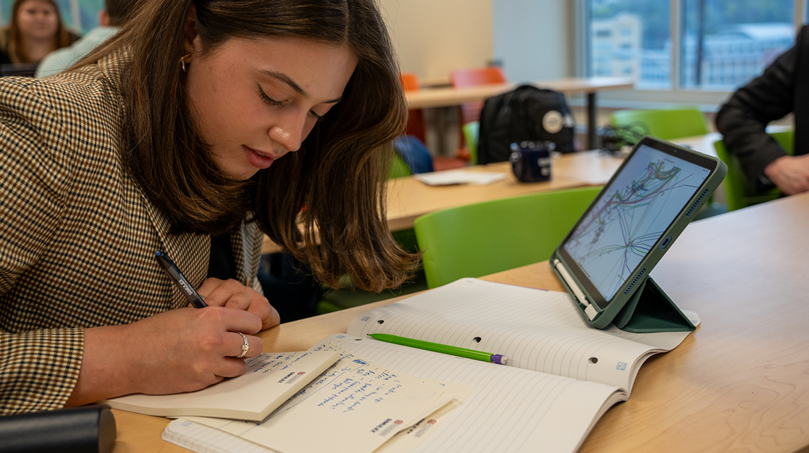 Student takes notes from map that's seen on her tablet.