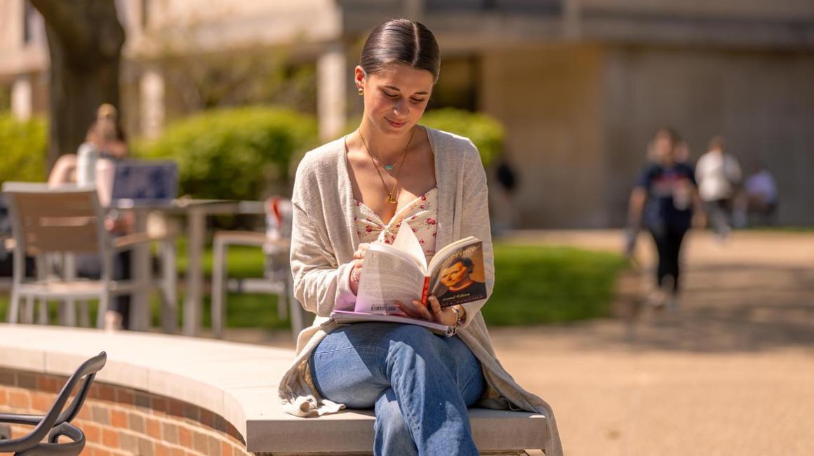 Student reading book near Unico Pavilion