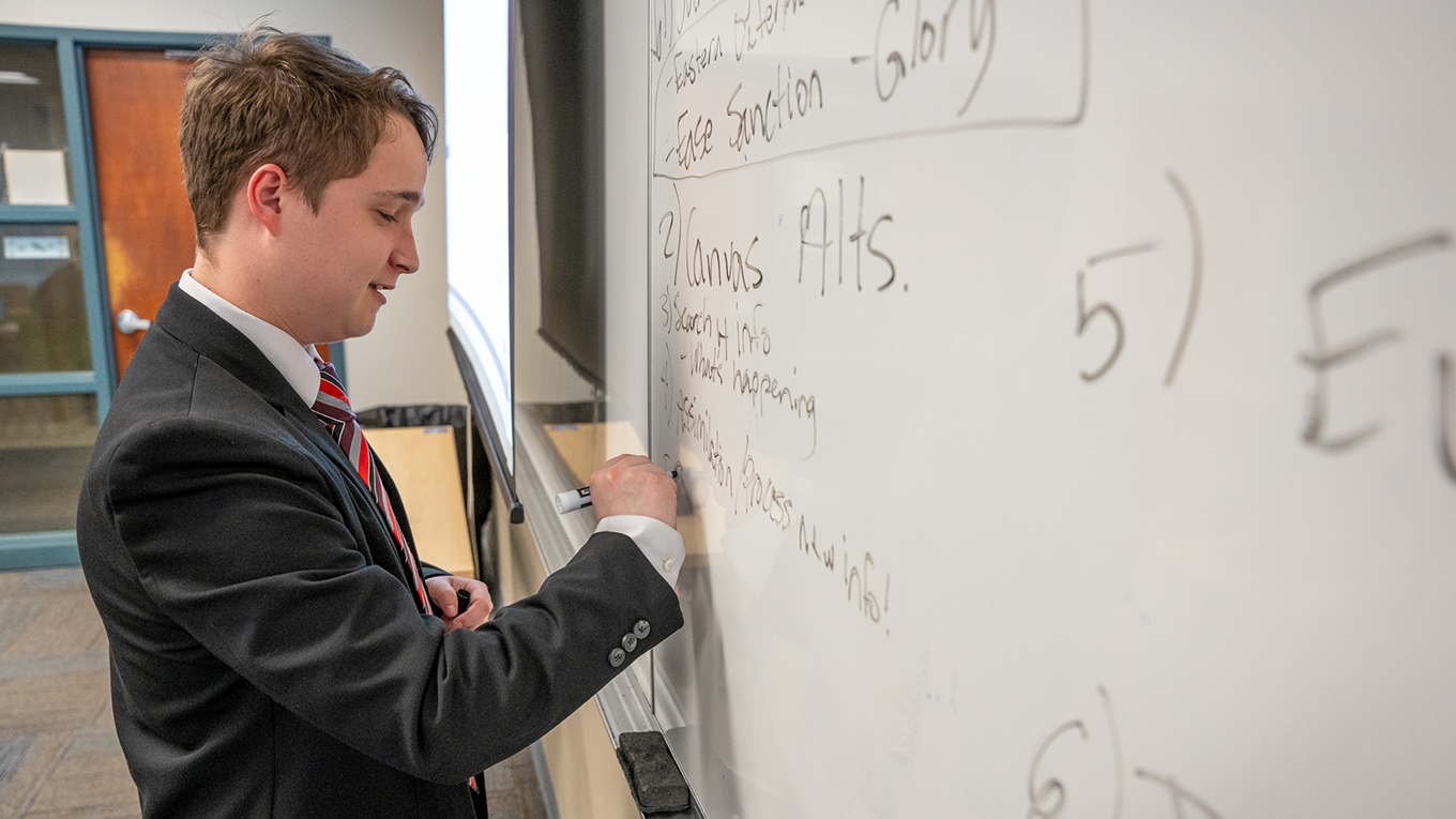 Student writing down rhetorical plan on whiteboard.