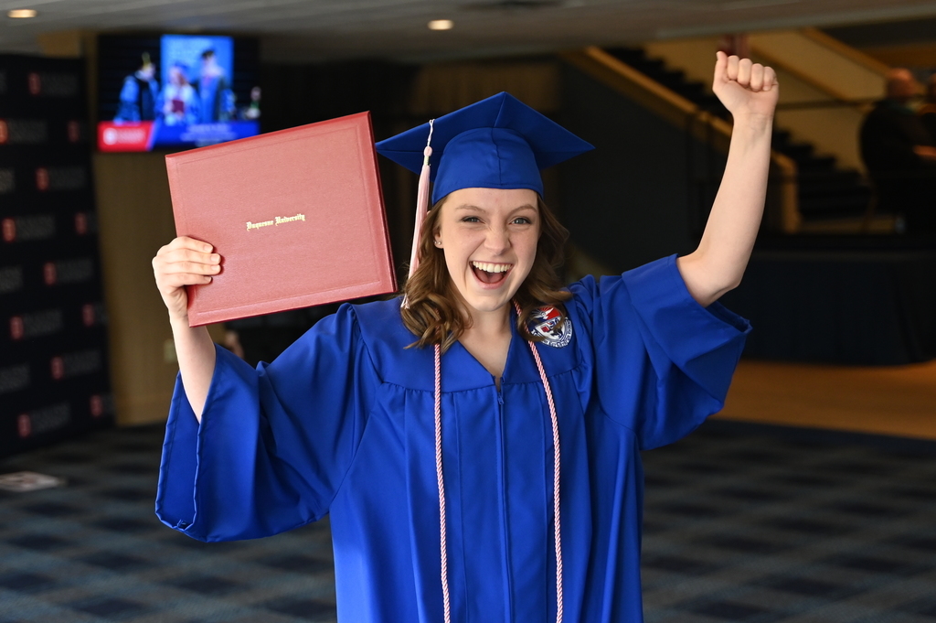 A graduting student celebrates with diploma cover in hand.