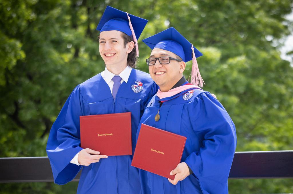 Two graduates wearing academic regalia smile holding red Duquesne Unviersity diploma covers.