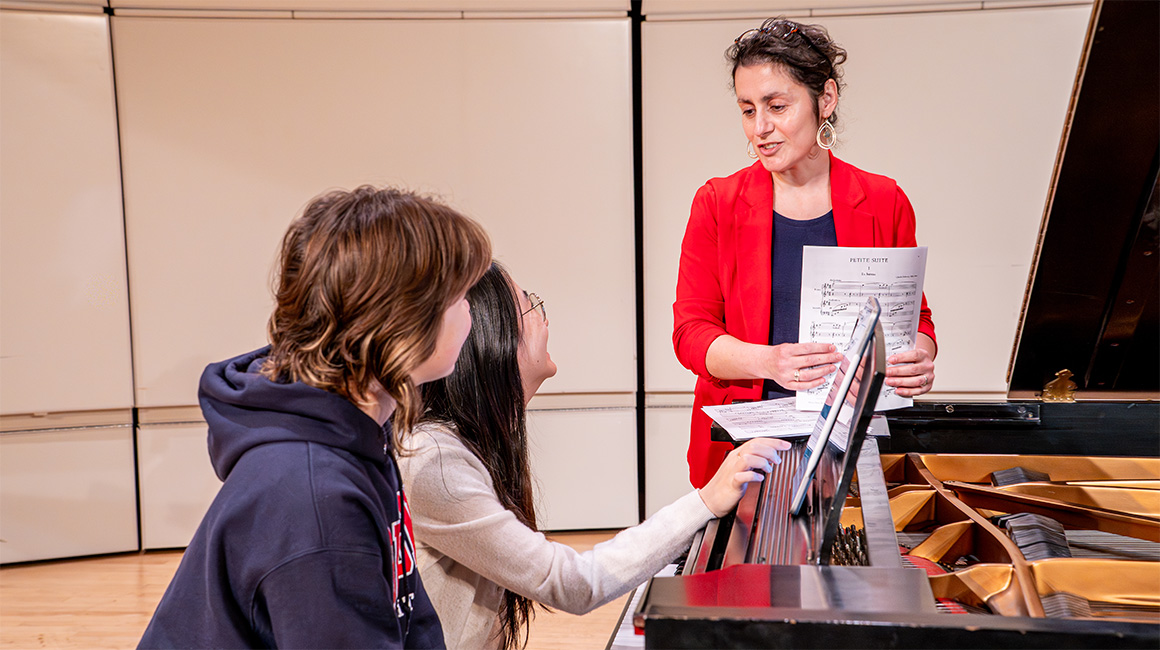 Students laughing and playing piano with a professor who is also smiling.