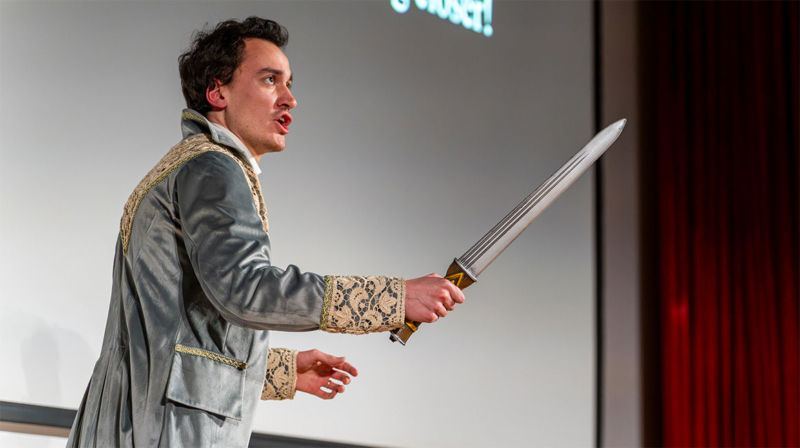 A person in costume holds a sword and sings on stage.