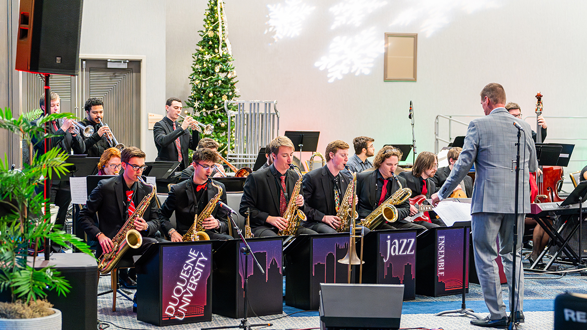 Jazz ensemble performs on stage with brass and saxophones during holiday concert.