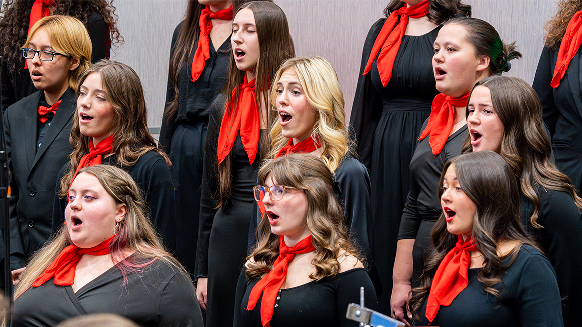 Choir members singing in black attire with red scarves during holiday program.