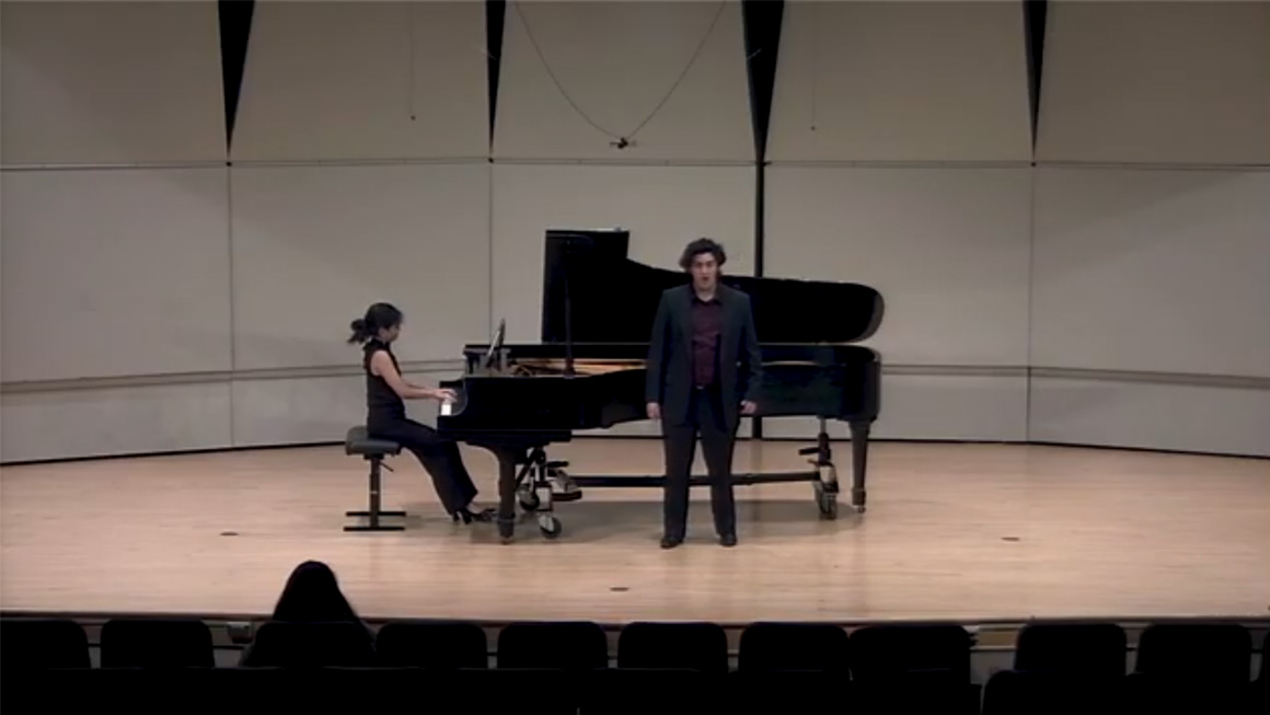 A person sings on a stage with a pianist accompanying.