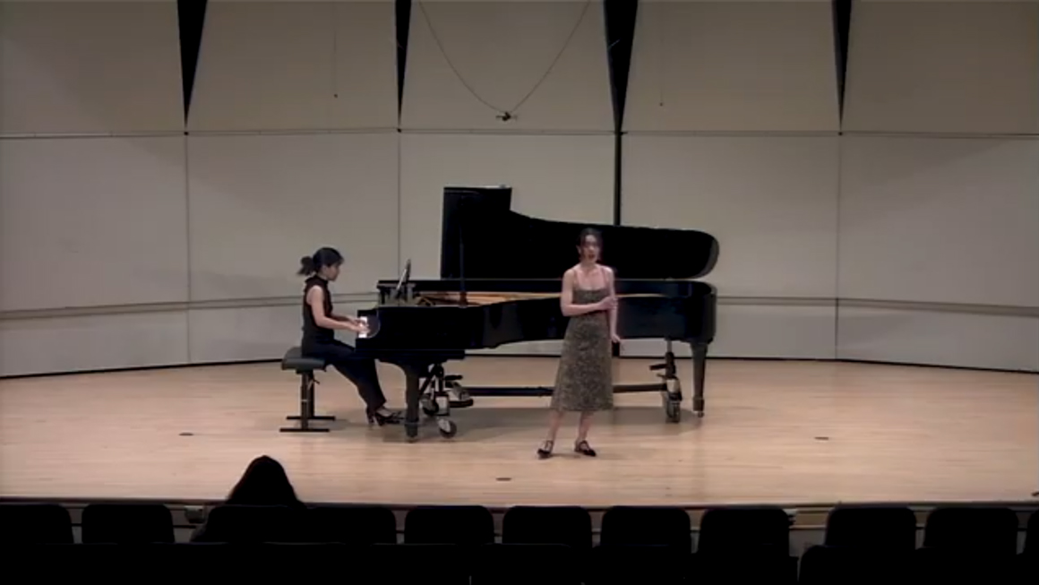 A person sings on stage with a pianist.