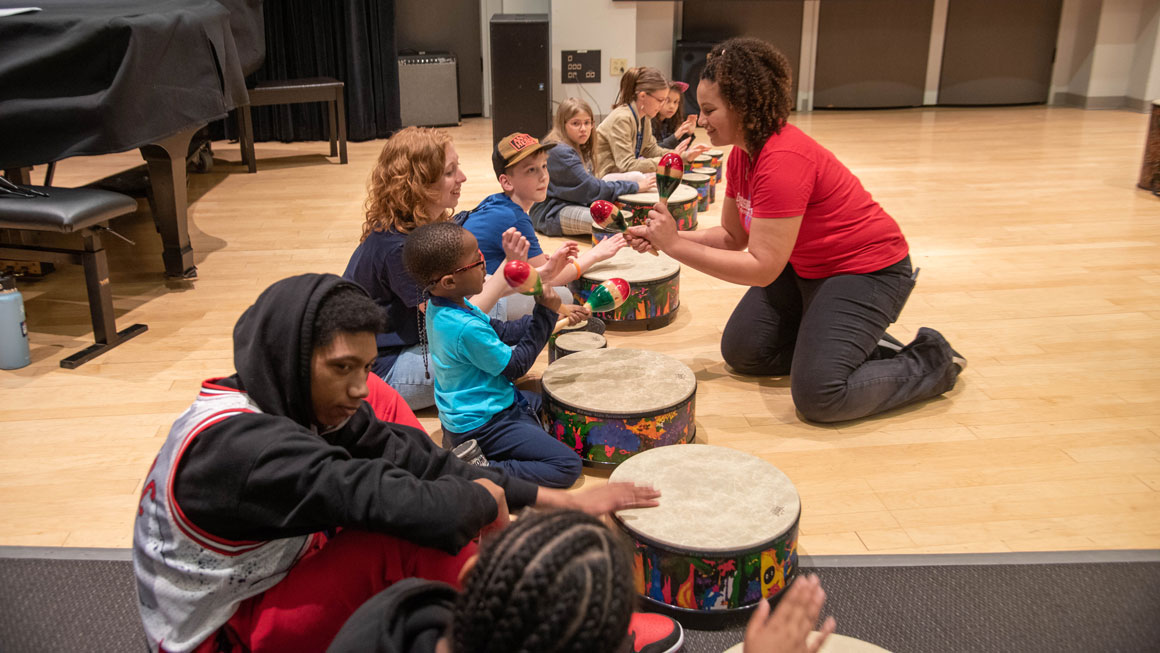 A student working with younger children at a drum circle.