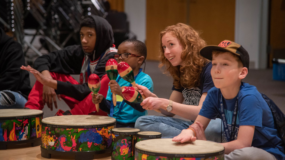 A student working with younger children at a drum circle.