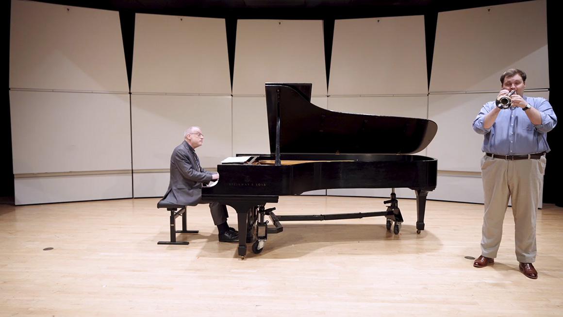 A trumpet player and a pianist perform together on stage.