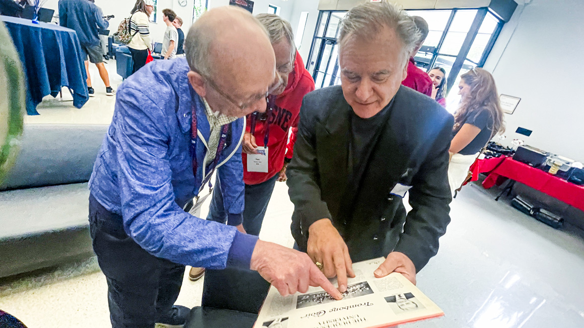 Three people gather around a vinyl record recording. They point at the image on the back cover of the record.