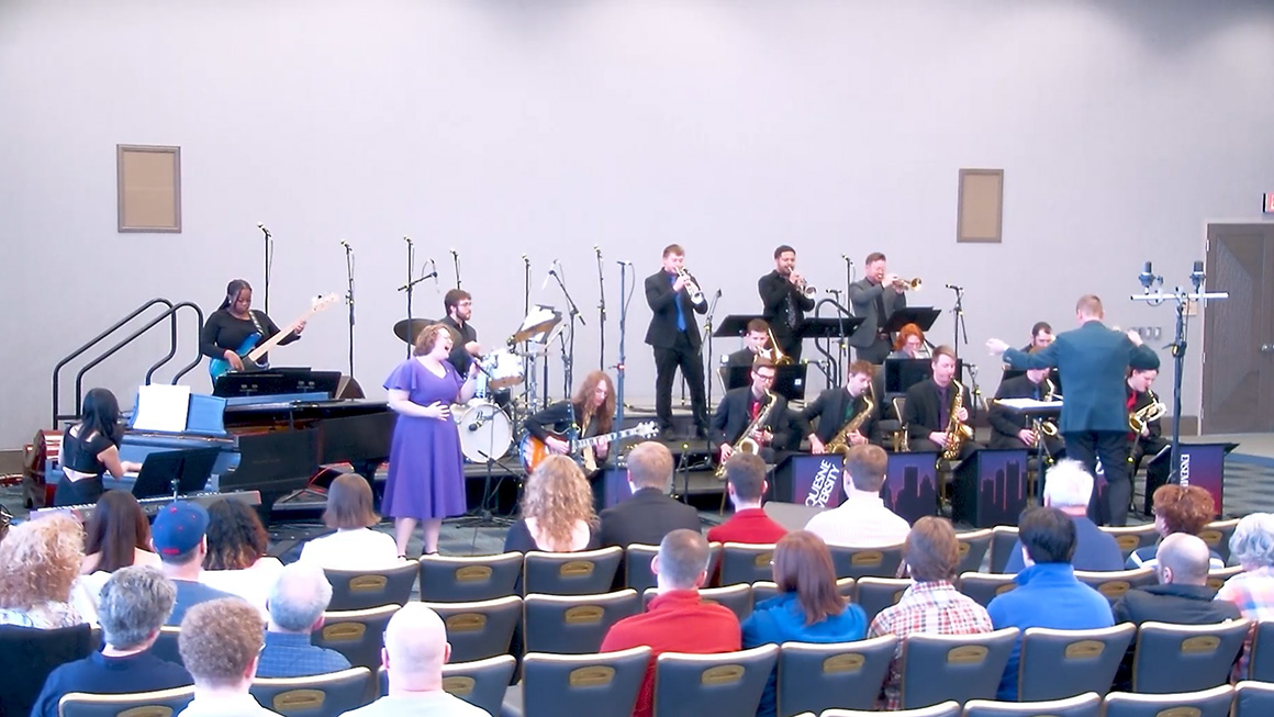 A jazz ensemble performs on a stage in front of a seated audience.