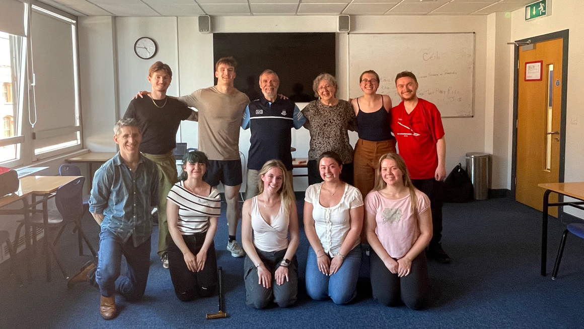 Students and faculty pose together in a classroom following a guest presentation, smiling for a group photo in front of a whiteboard and large display screen.