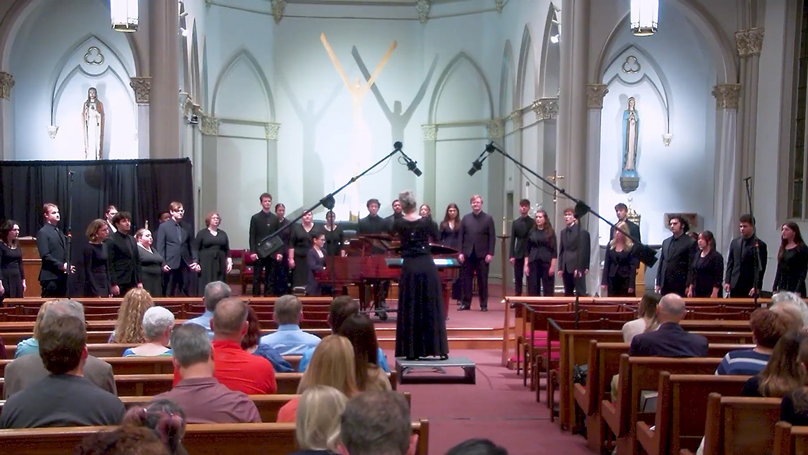 A choir performs on the altar of a church in front of an audience seated in the pews.