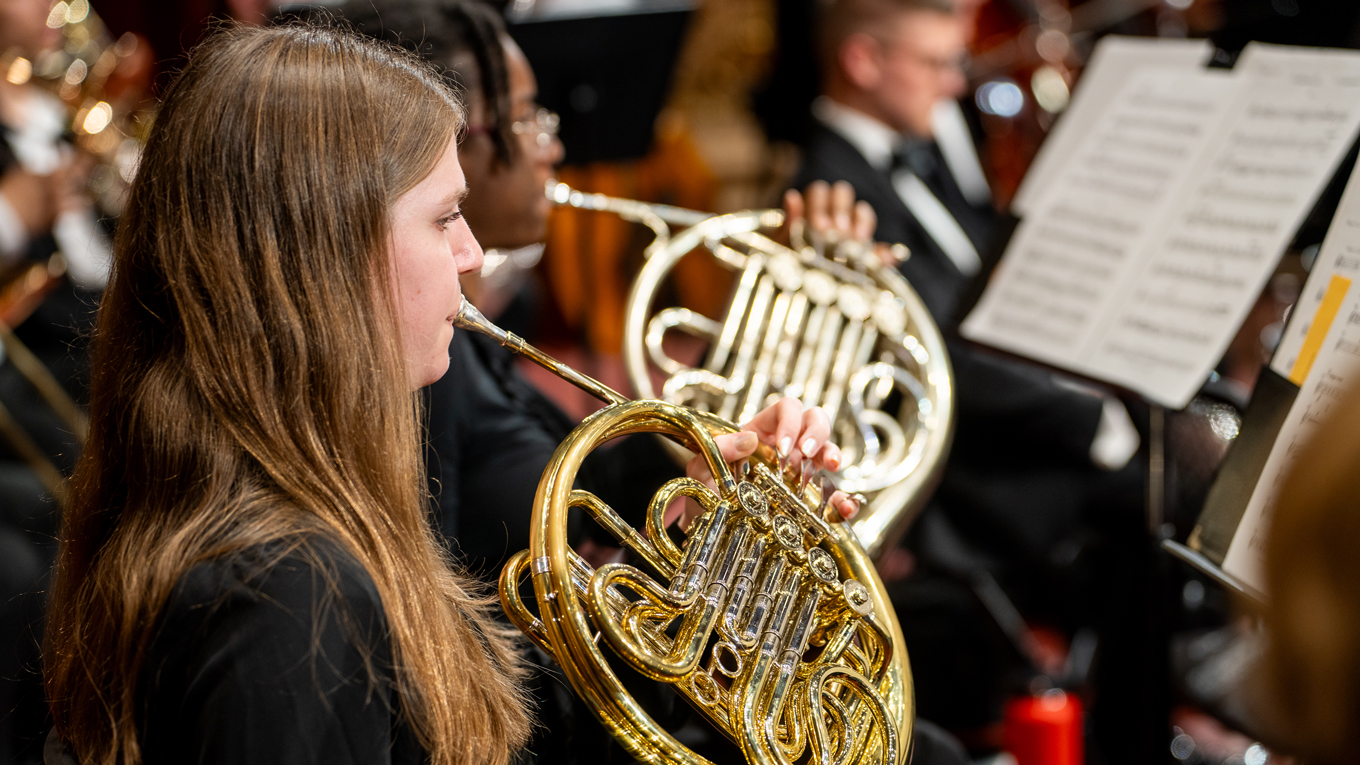 A horn player performs on stage.