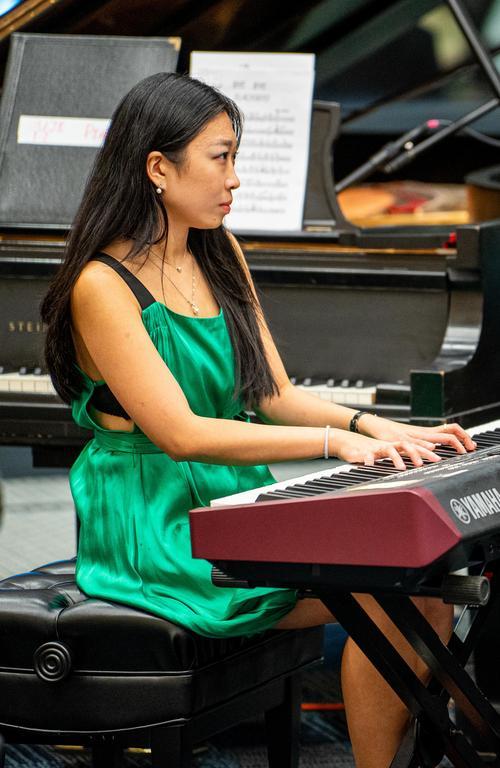 A person in a greed dress performs on an electronic keyboard with a Steinway grand piano in the background.