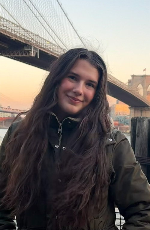 A person wearing a coat stands in front of a bridge.