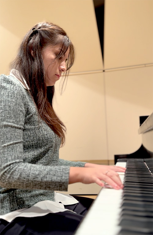 A person wearing a gray sweater plays the piano.