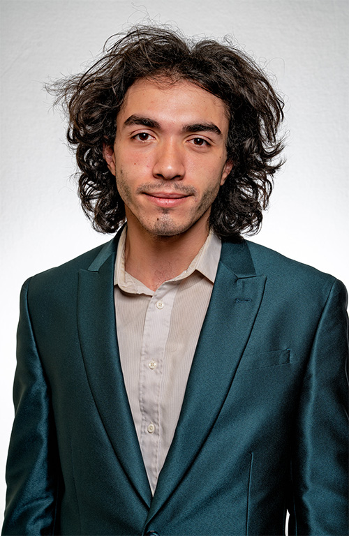 A person earing a blue suit jacket poses for a portrait in front of a neutral background.