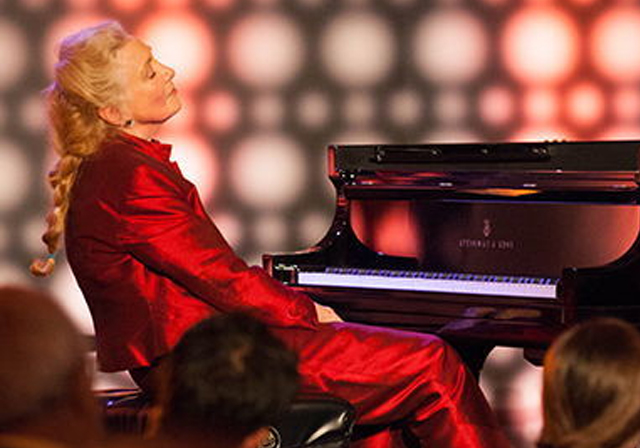 A person in red sits at a piano.