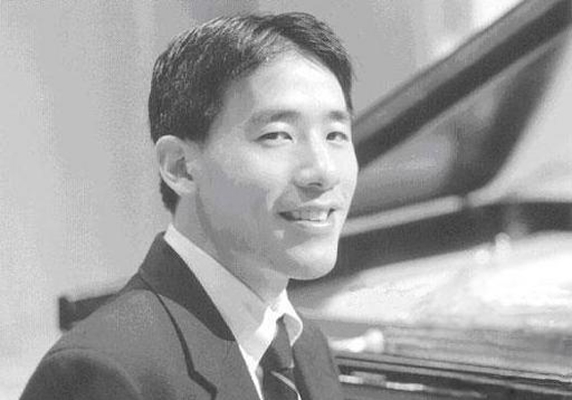 Black and white portrait of a person smiling in front of a piano.