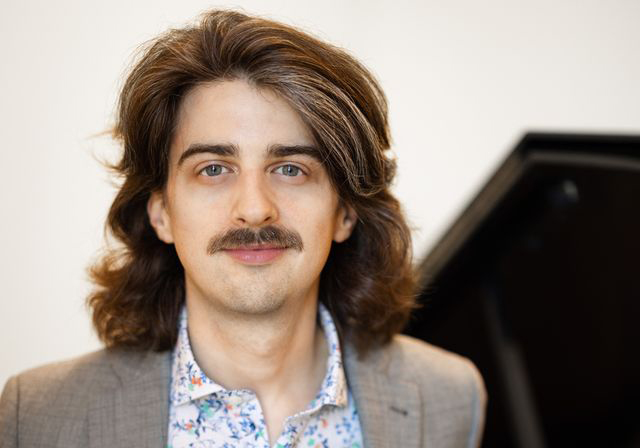 A person smiles in front of a piano.