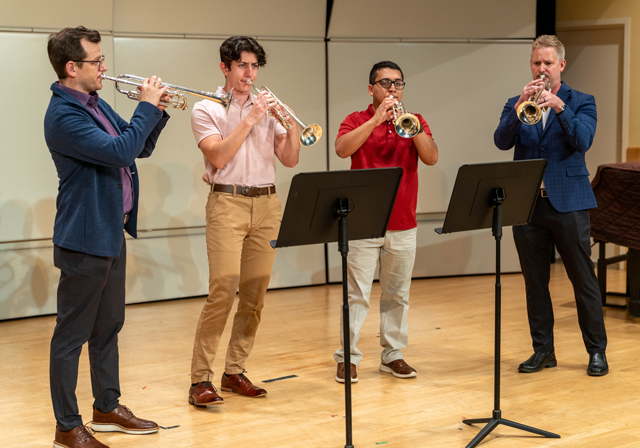 Four people play trumpets.