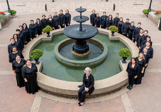 A group of people wearing black pose for a photo around a circular fountain.