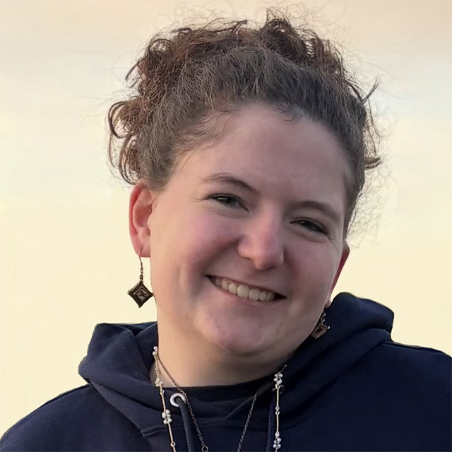 Student smiles in front of a tan background.