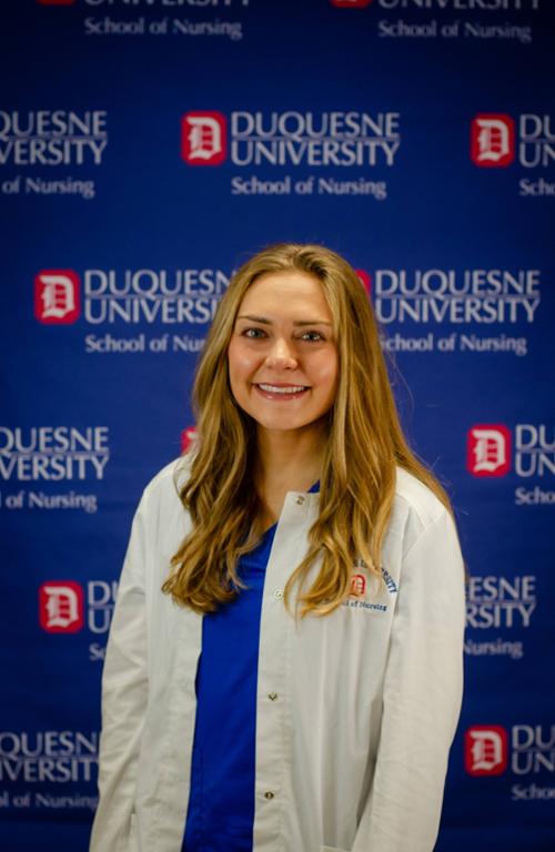 female nursing student standing with her scrubs and white coat on