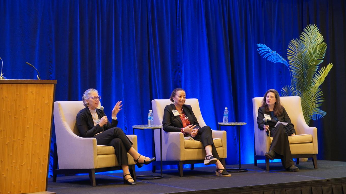 Three speakers engage in discussion at a health care conferece.