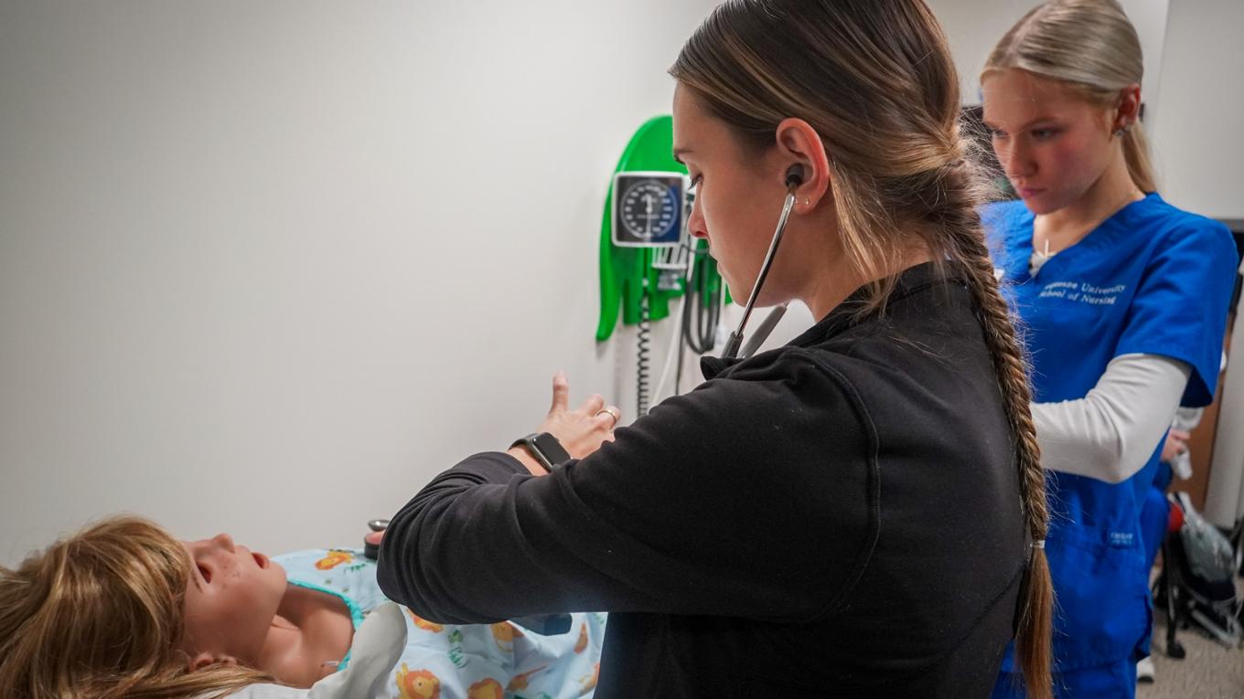 A nursing student practices on a pediatric mannequin.