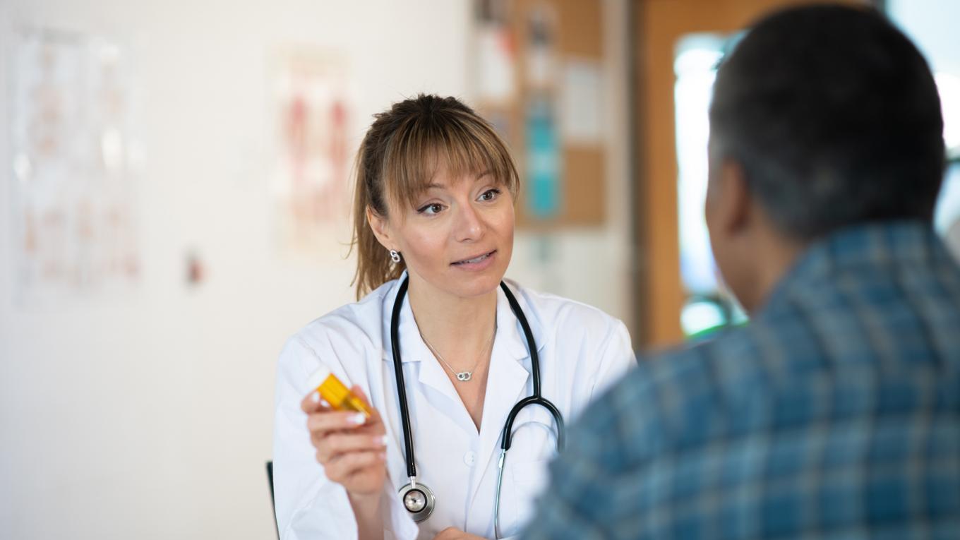 A health care worker holding a pill bottle discusses medication with their patient. 