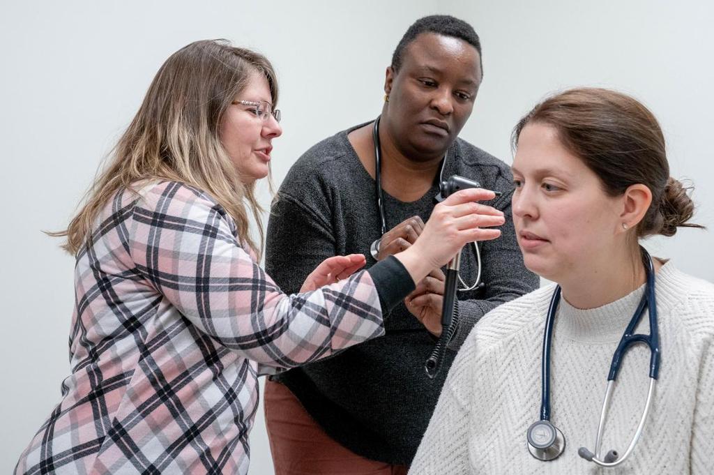 A teacher showing a woman how to use an otoscope on another student. 