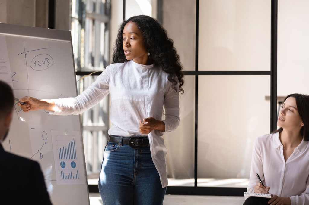 woman presenting at white board while two other people watch