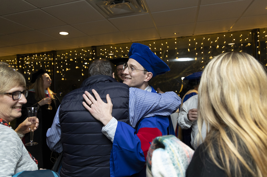 a male in a cap and gown hugging someone with a puffy vest