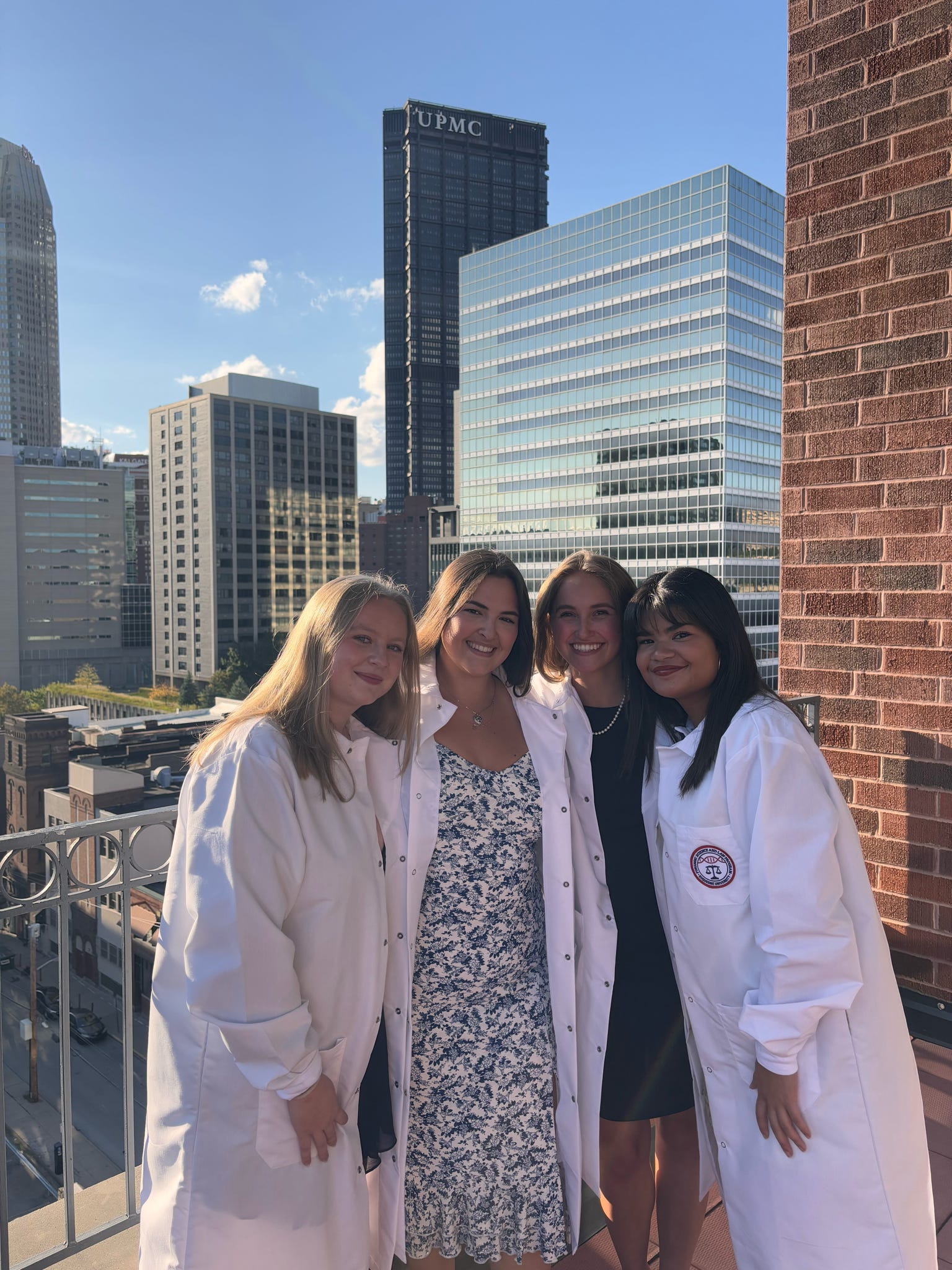 four girls in front of tall buildings wearing white coats