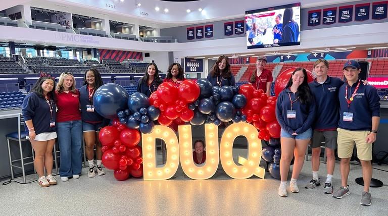 Duq day student ambassadors in from of ballons and a light up D-U-Q.